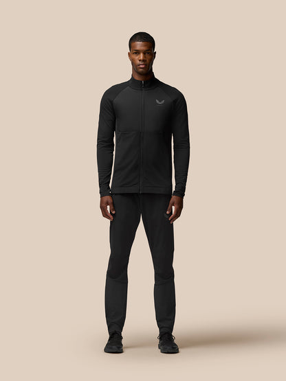 Full body shot of a male model wearing Flow Training Jacket black with matching pants against a beige backdrop