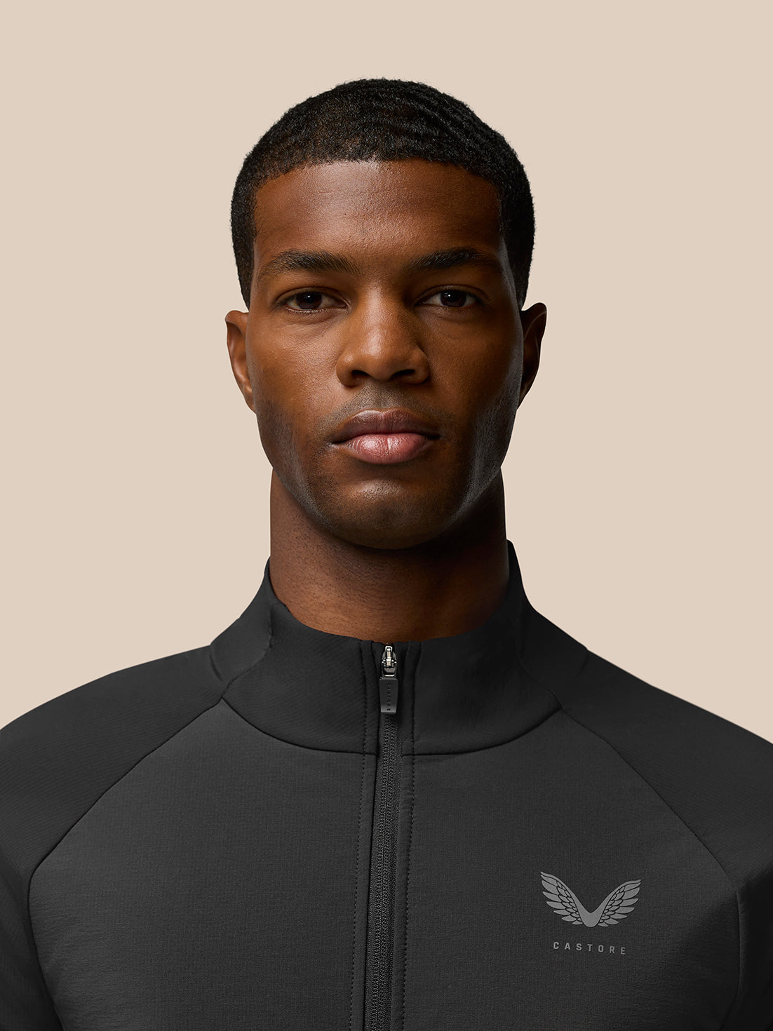 Close up of a male model wearing Flow Training Jacket in black with front zipper and Castore logo on the chest