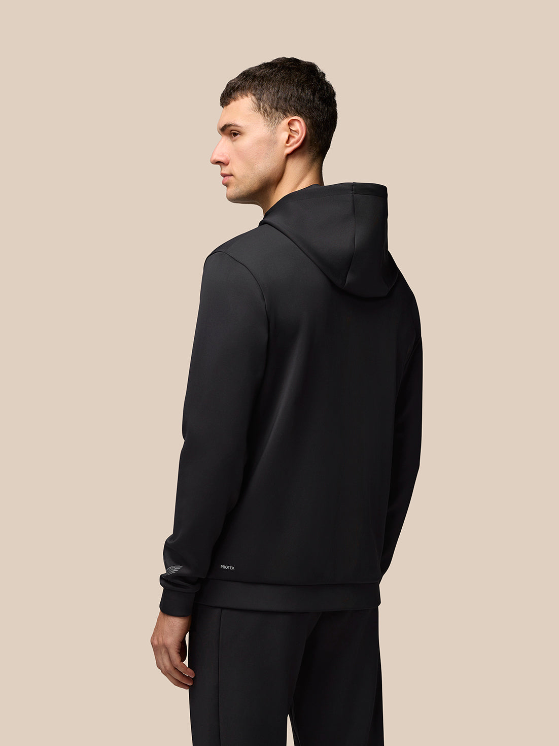 Three-quarter back view of a man wearing a black Flex Lifestyle Full Zip jacket with hood