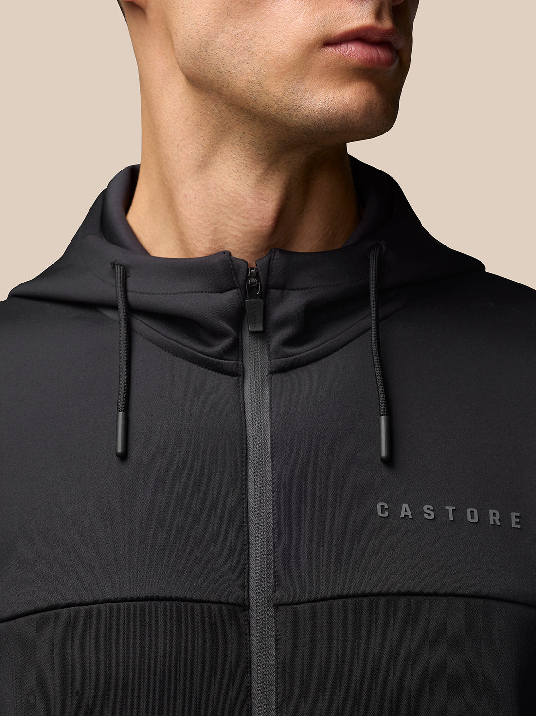 Front view of a man in a black hooded full-zip jacket with Castore logo on the left chest