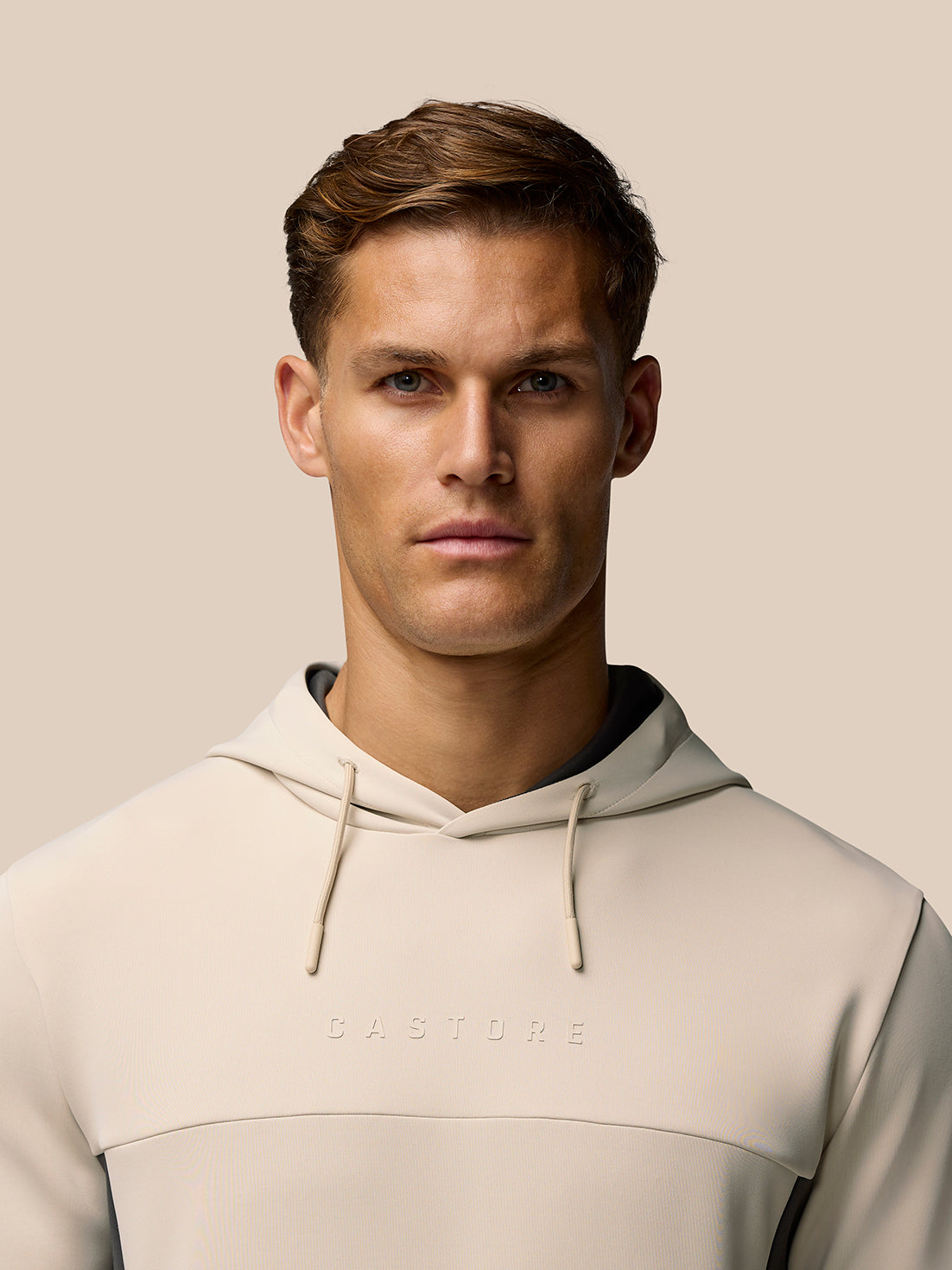 Front view of beige Flex Lifestyle Hoodie on a male model, hood up with drawstrings and chest branding
