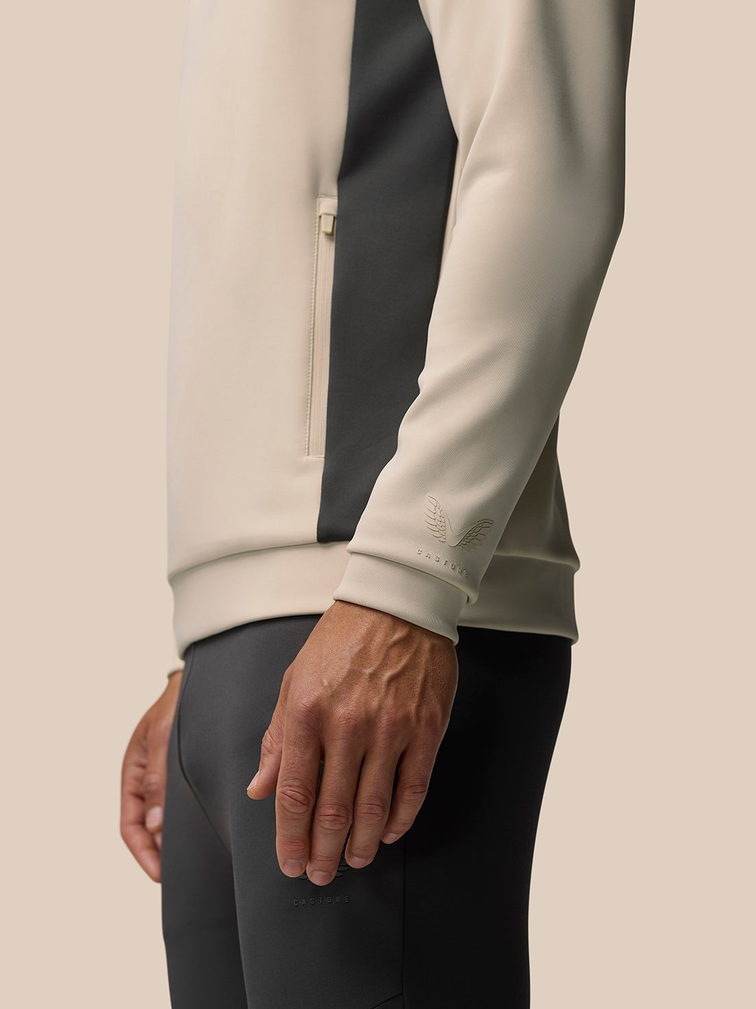 Side view of beige and black panel Flex Lifestyle Hoodie featuring side zip pocket and embossed Castore logo on cuff