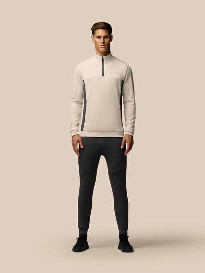 Male model wearing Beige Flex Lifestyle 1/4 Zip top with stand collar and zip pockets, paired with dark athletic pants