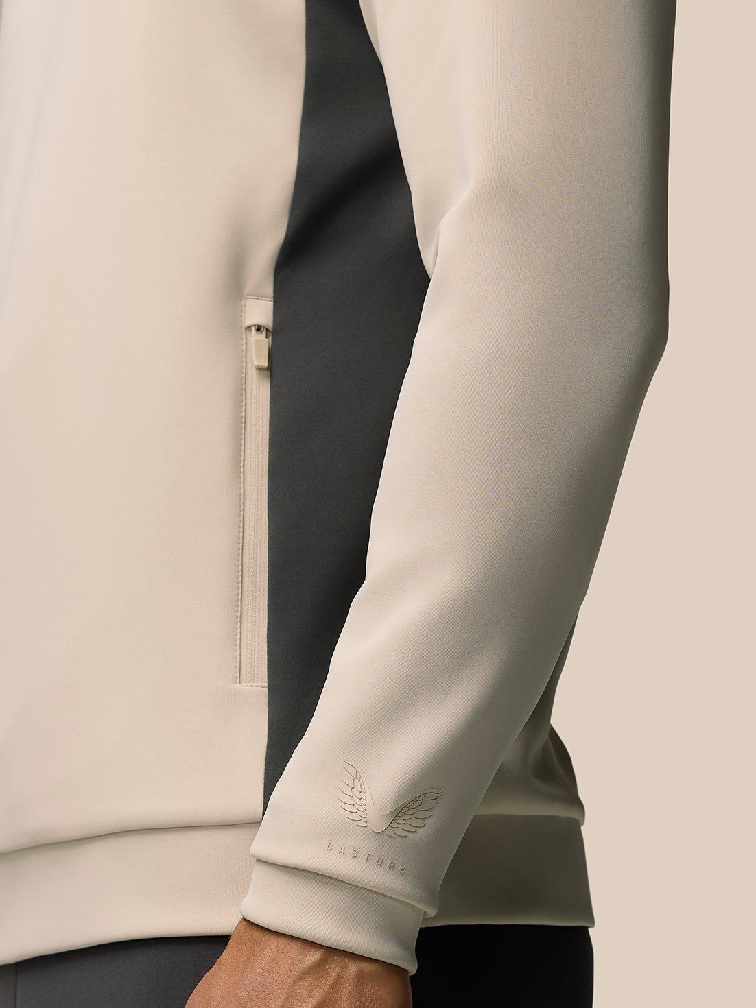 Close up of beige Flex Lifestyle 1/4 Zip top sleeve showing side panel, embossed Castore logo on cuff and zip pocket.
