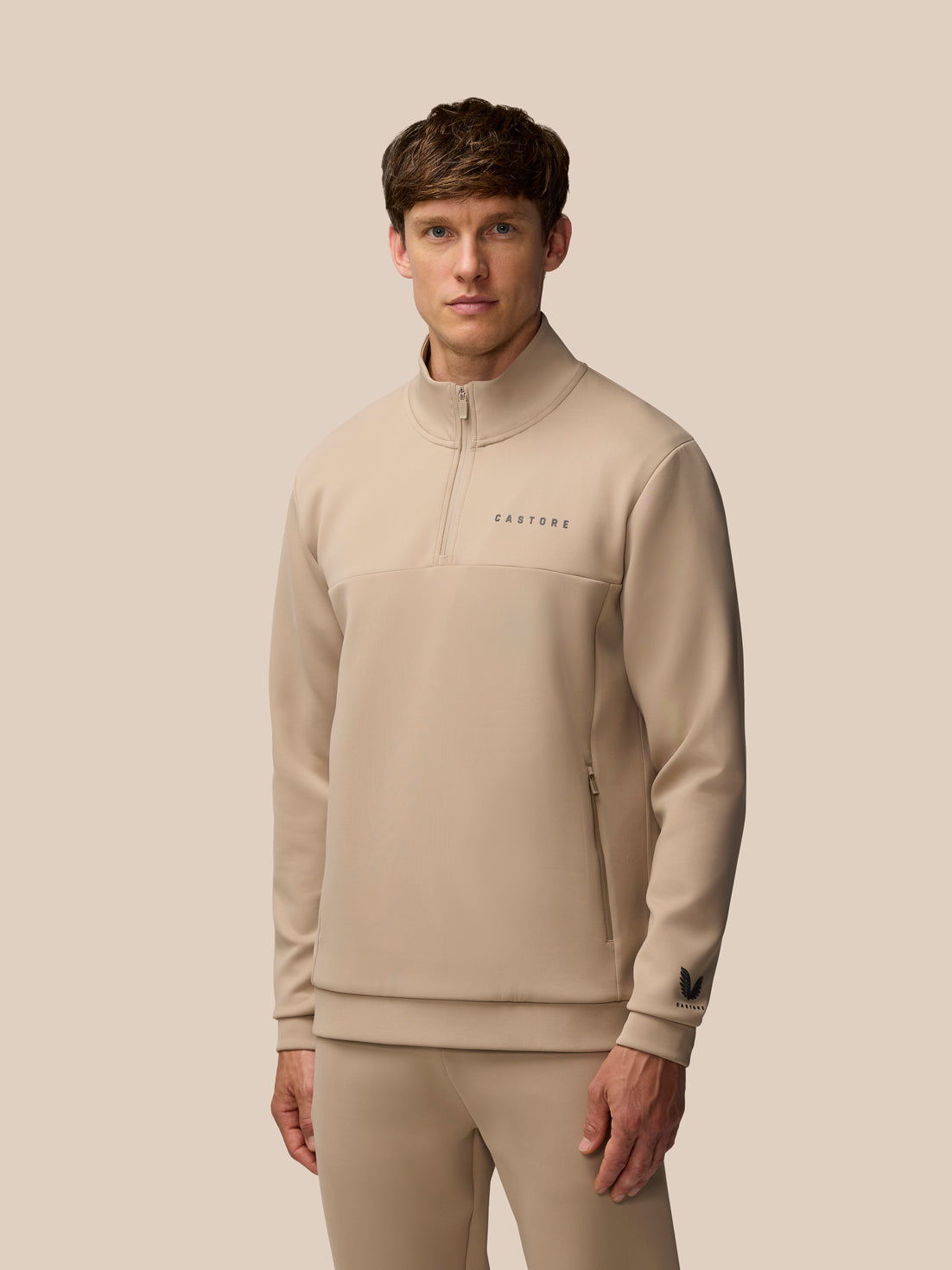 Male model wearing mushroom beige Flex Lifestyle 1/4 Zip top with centre front zip and Castore logo.