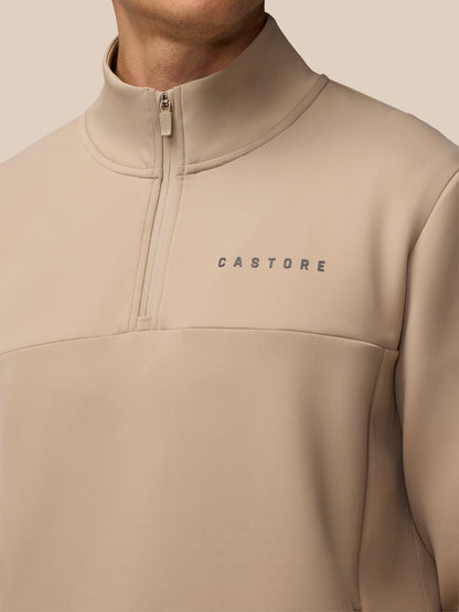 Beige half zip top with Castore wordmark on the chest and a high collar zip