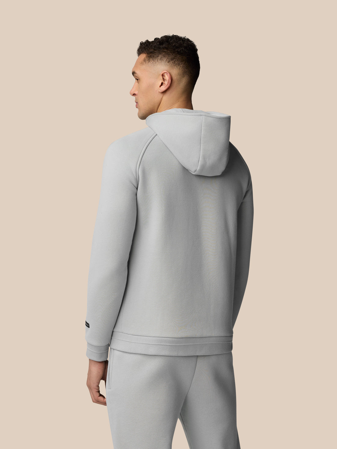Back view of a man in a light grey Adapt Fleece Zip-Through Hoodie with the hood down