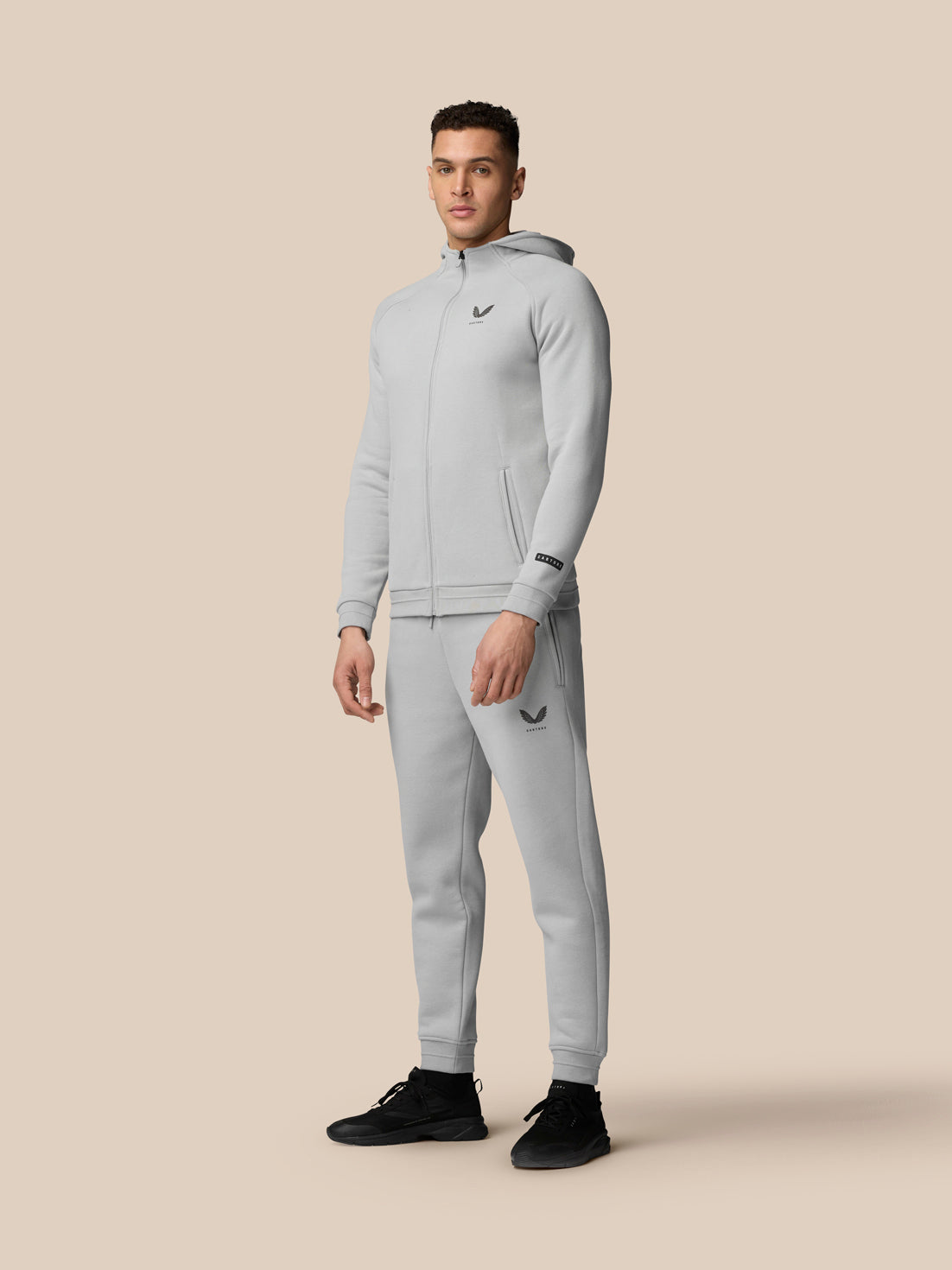 Full-body view of a model in grey Adapt Fleece Zip-Through Hoodie and matching joggers with Castore logos on chest and thigh.