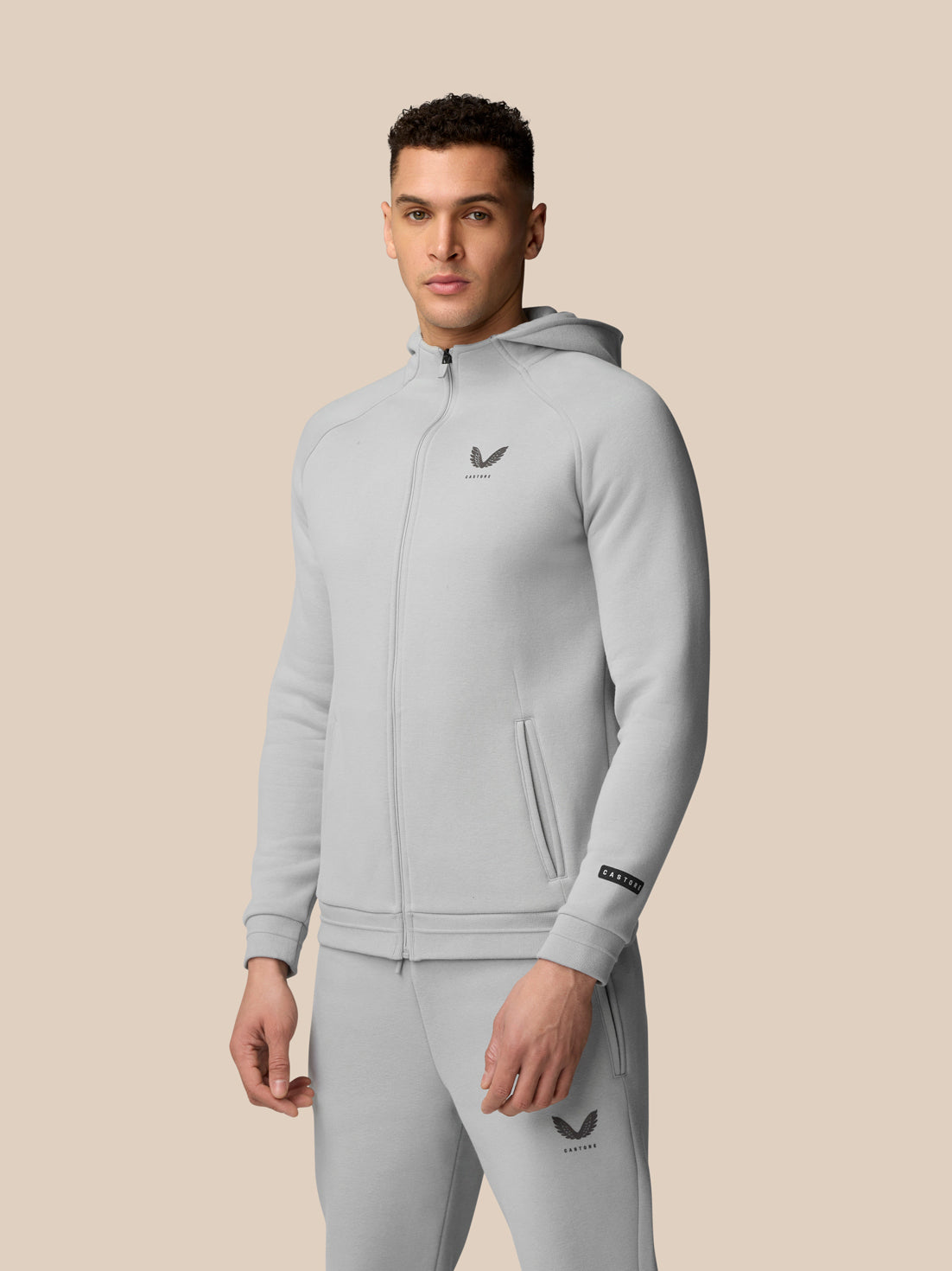 Man in light grey Adapt Fleece Zip-Through Hoodie with hood front pockets and Castore logo on chest.