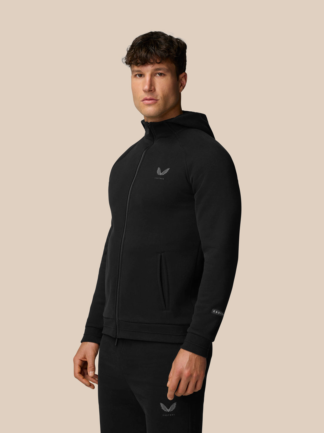 Male model wearing black Adapt Fleece Zip-Through Hoodie with front pockets and subtle logo