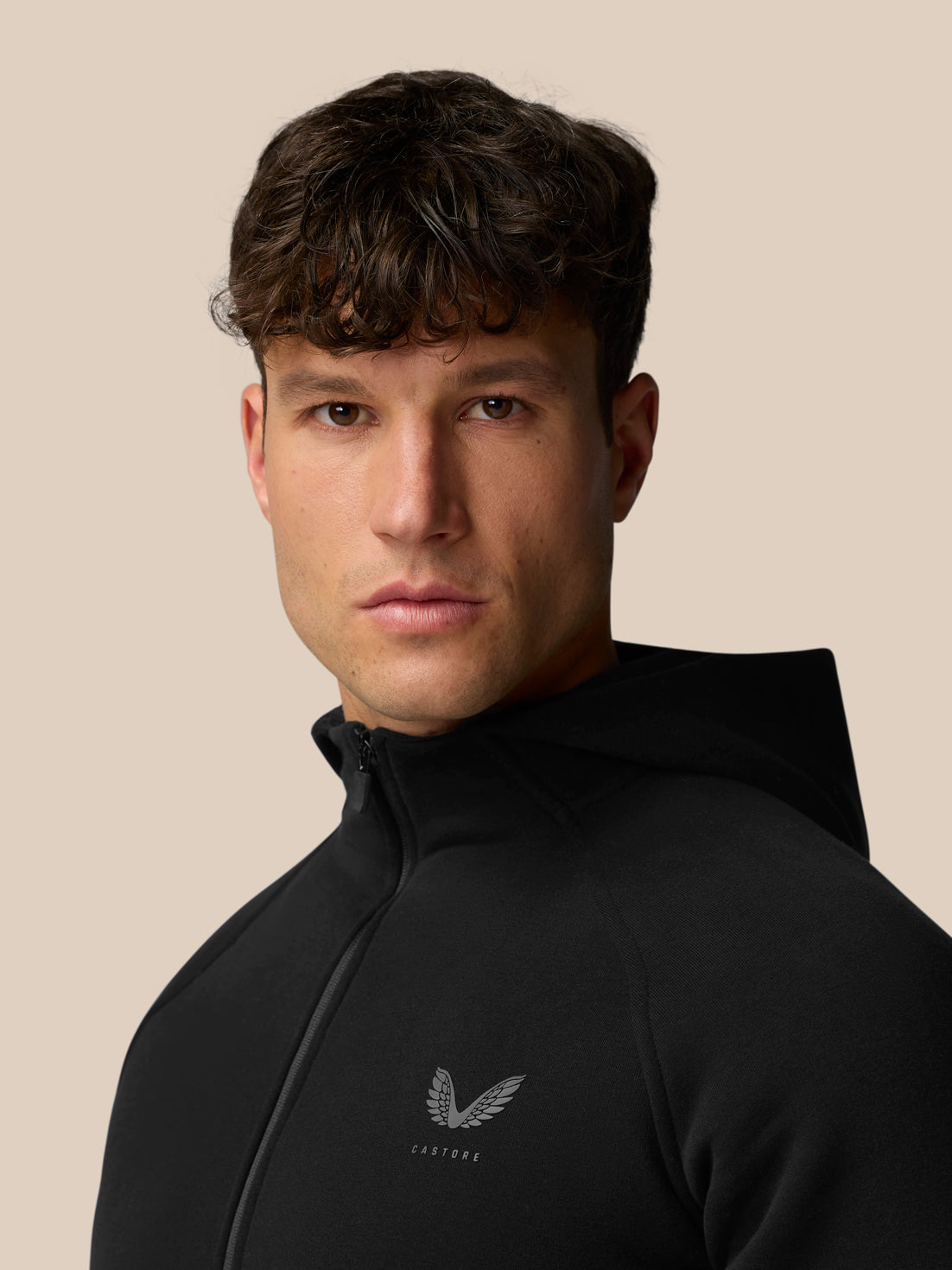 Three-quarter view of a man in a black hooded zip hoodie showing the Castore chest logo