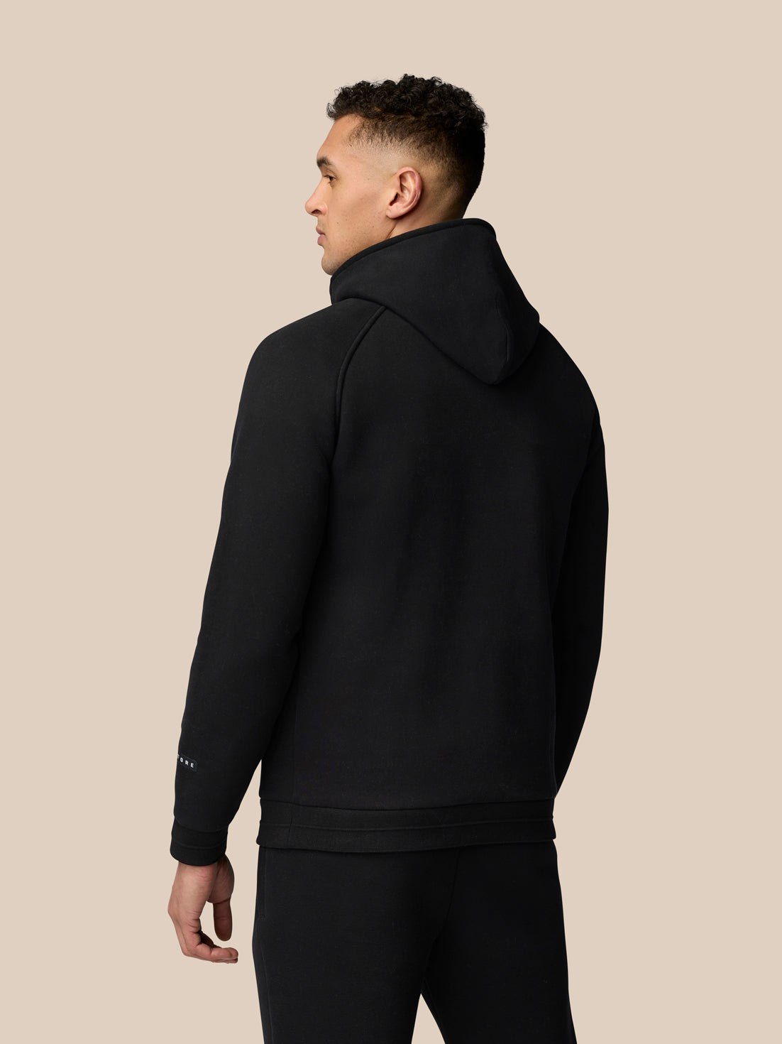 Back view of a model wearing a black Adapt Fleece Hoodie with hood up and clean silhouette