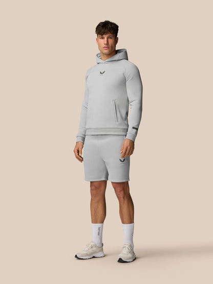 Male model in light grey Adapt Fleece Hoodie with matching shorts and visible chest and leg logos against beige backdrop