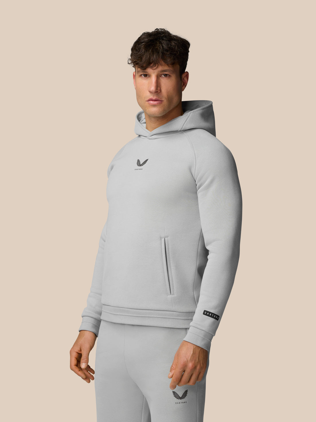 Model wearing light grey Adapt Fleece Hoodie with hood down, chest logo and front pocket visible.