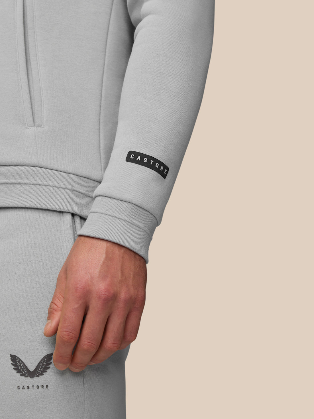 Model wearing grey Adapt Fleece Hoodie showing zip pocket and brand label on sleeve