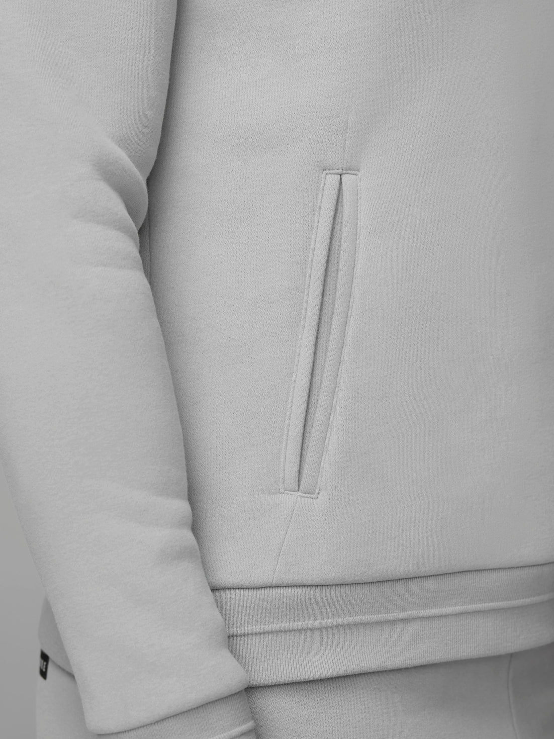 Close-up of a vertical zippered pocket on a light grey fleece hoodie.