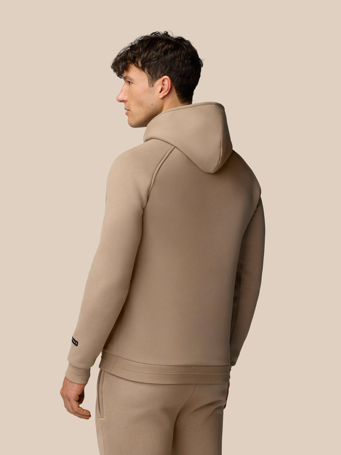 Back view of a male model wearing clay Adapt Fleece Hoodie showing the hood and clean seam lines.