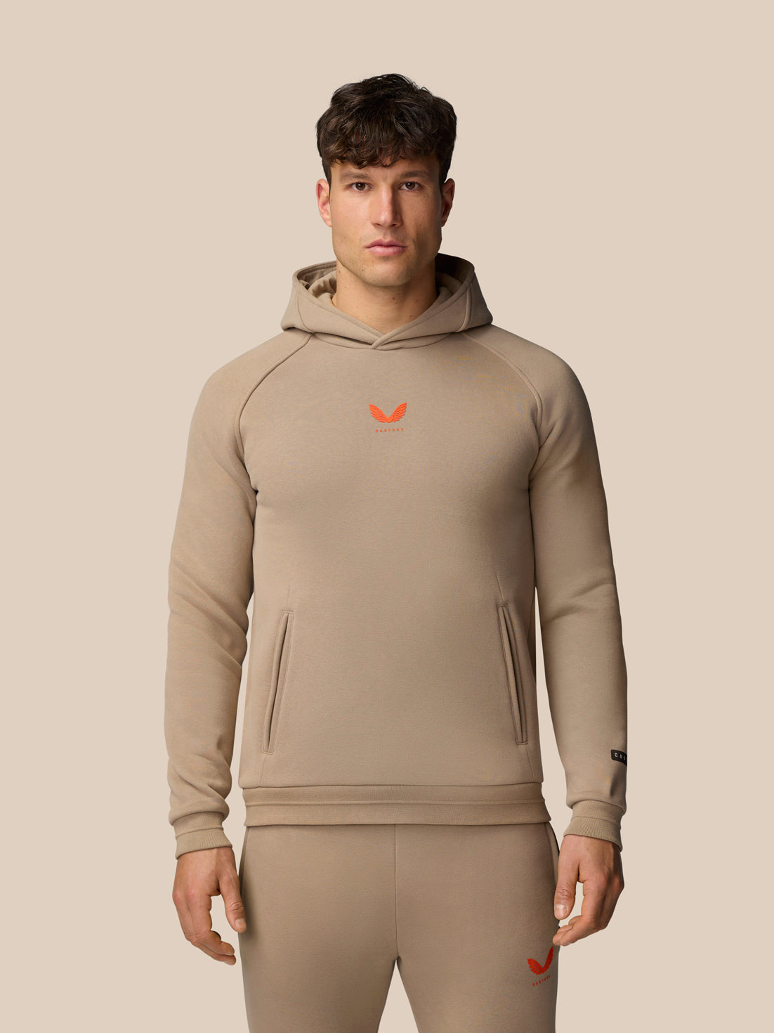 Front view of a male model wearing clay Adapt Fleece Hoodie with open front pocket high build collar and subtle branding.
