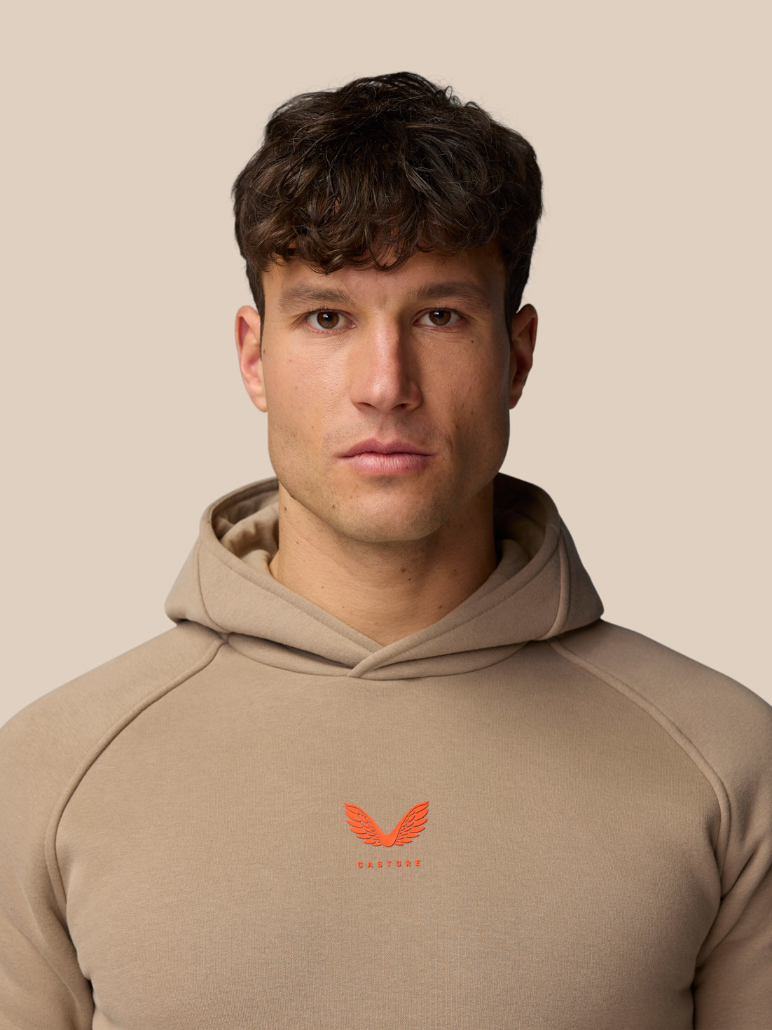 Clay colored Adapt Fleece Hoodie on a male model with hood down and an orange logo on the chest.