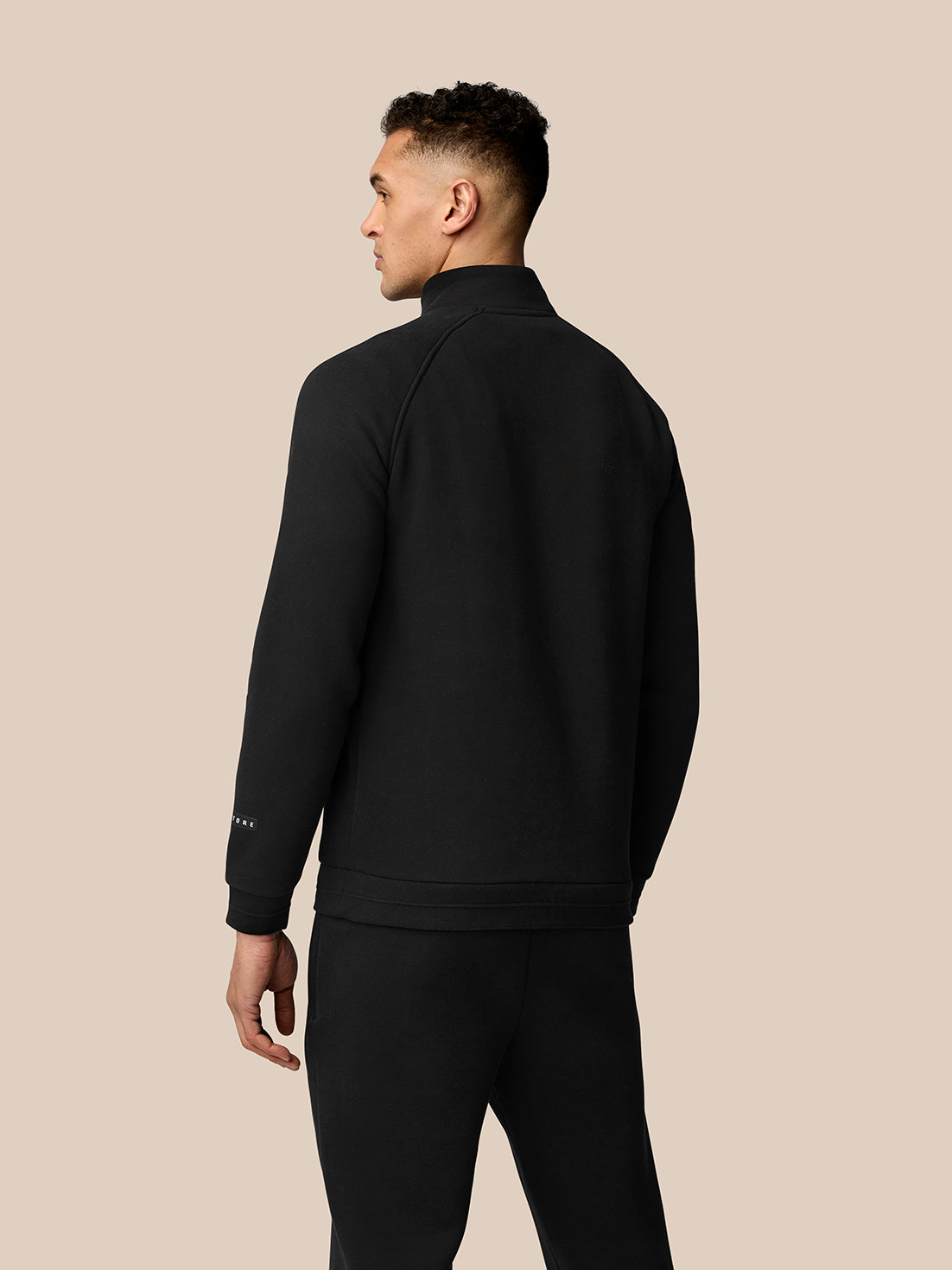 Back view of a man wearing a black Adapt Fleece Quarter Zip jacket with a clean silhouette and minimal branding.