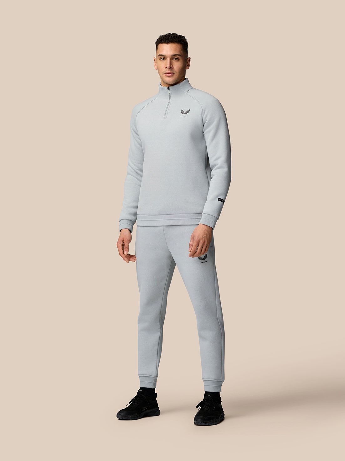 Male model wearing light grey Adapt Fleece Quarter Zip top with matching joggers against a beige background