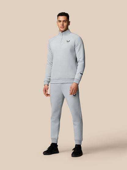 Male model wearing light grey Adapt Fleece Quarter Zip top with matching joggers against a beige background