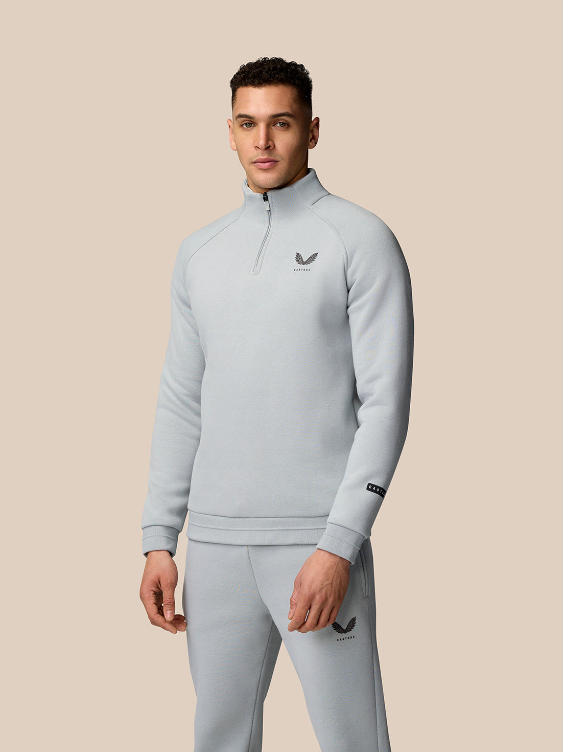 Full upper body shot of a male model in a light grey Adapt Fleece Quarter Zip with high build collar against a beige background.