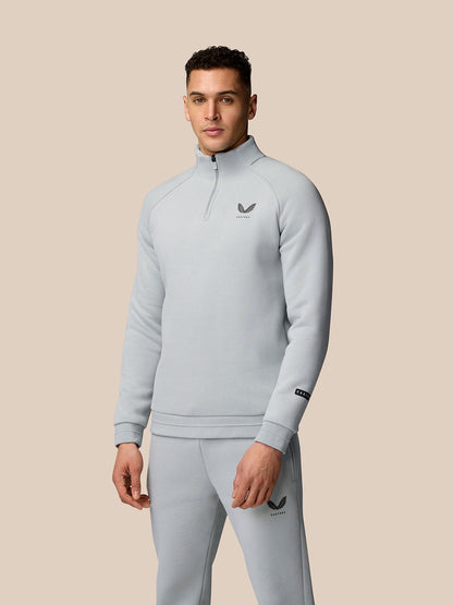 Full upper body shot of a male model in a light grey Adapt Fleece Quarter Zip with high build collar against a beige background.
