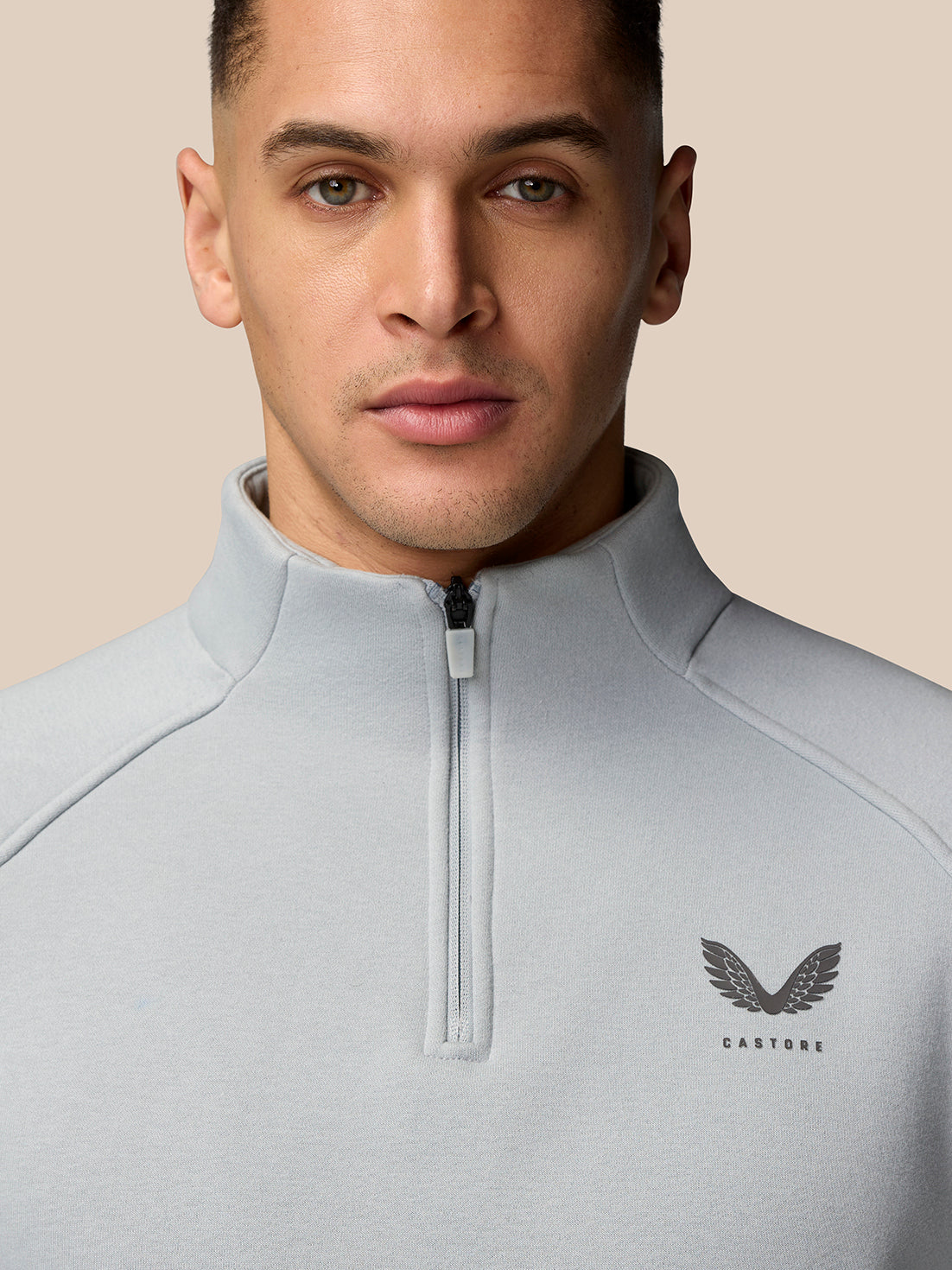 Close-up of a male model wearing a light grey Adapt Fleece Quarter Zip, highlighting the front zip and subtle chest logo.