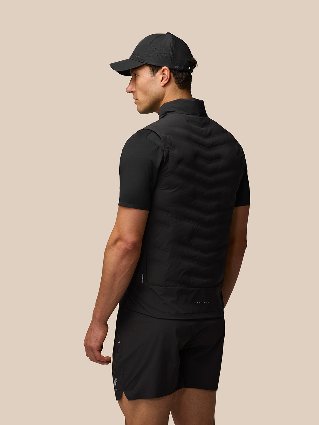 Model from behind wearing black Zone Training Gilet with padded sleeveless silhouette and reflective branding on the lower back