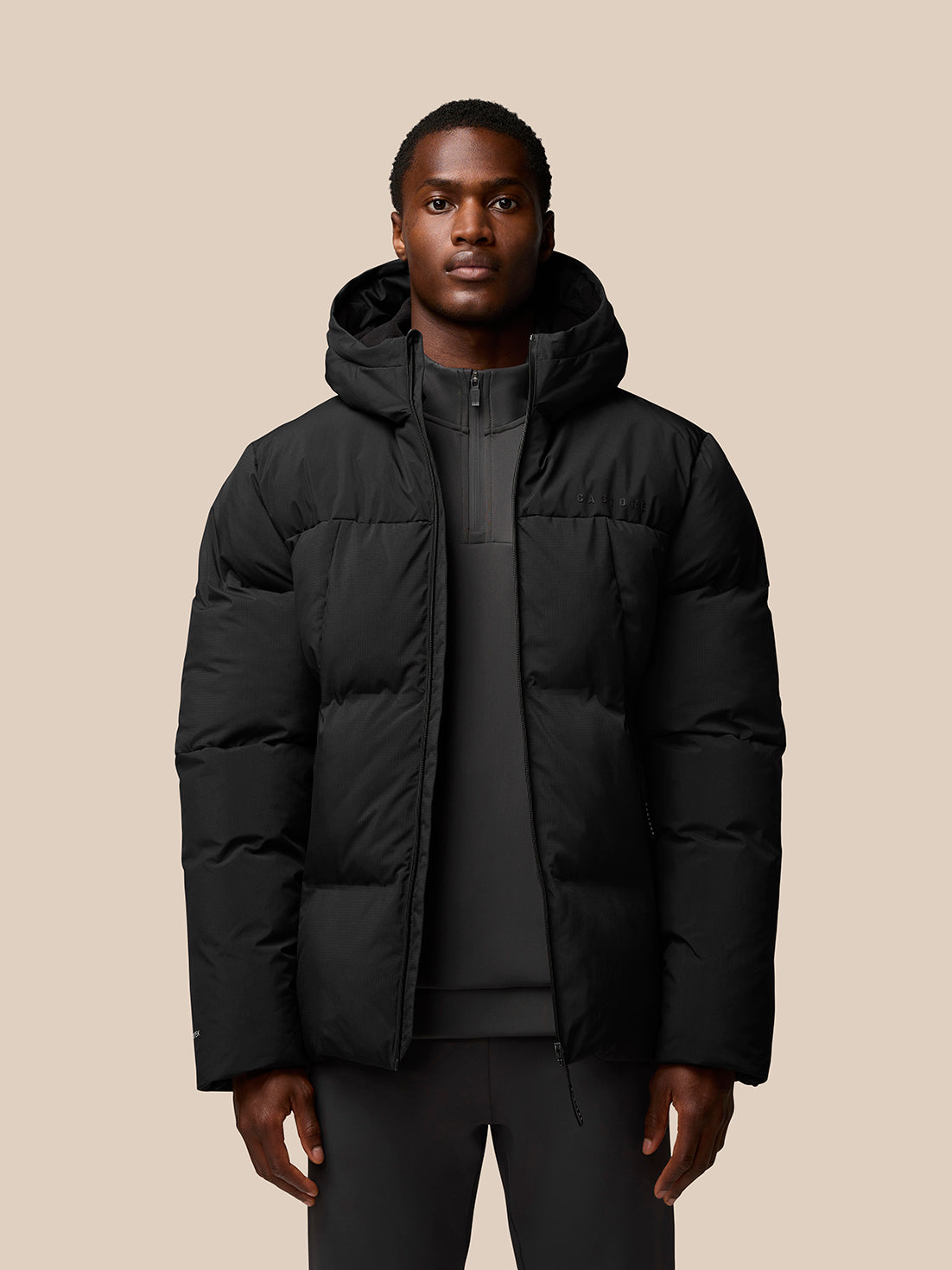 Male model wearing a black hooded puffer jacket with front zip and ProTek branding on the sleeve.
