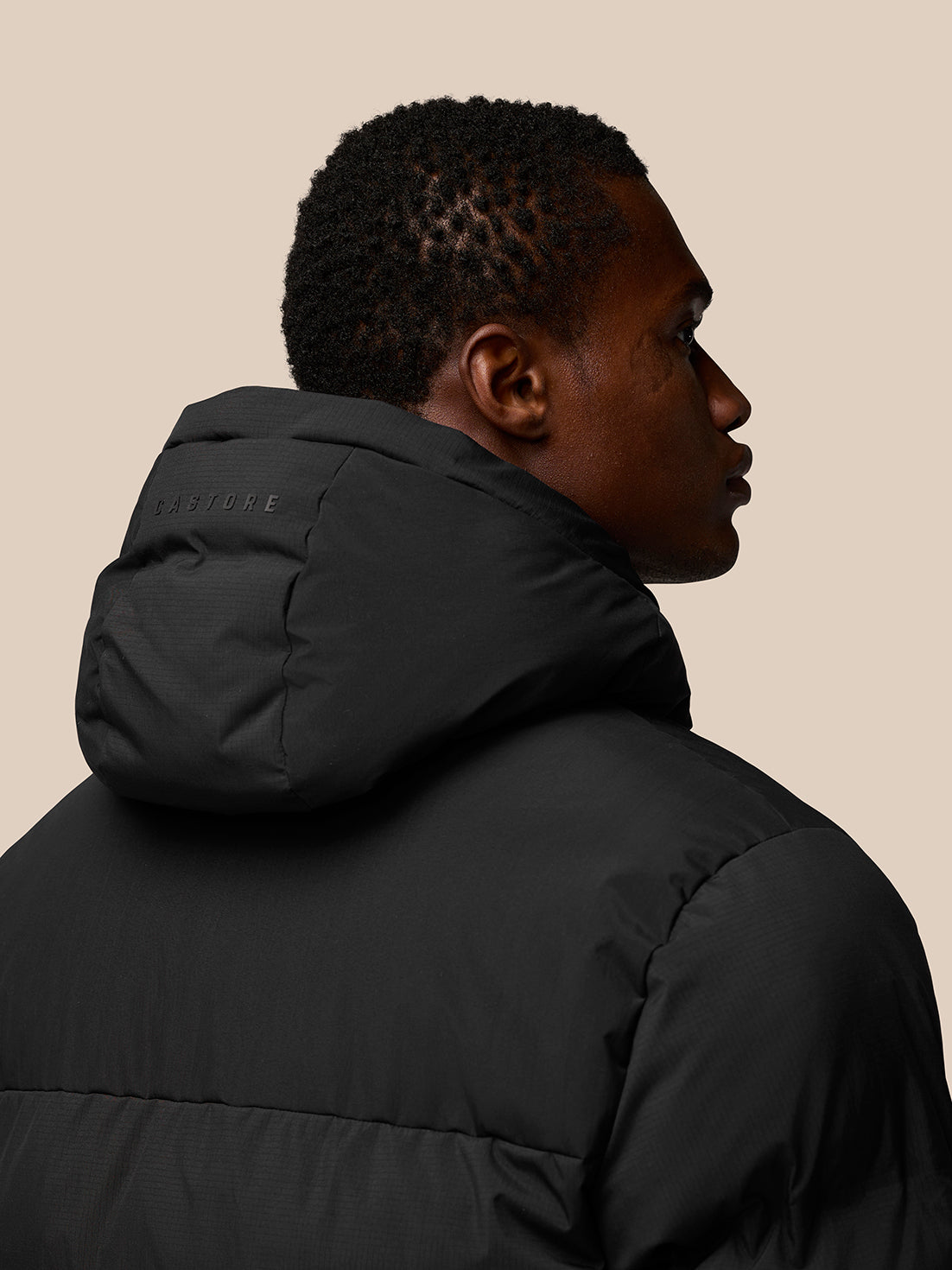 Back view of a man wearing a black Castore puffer jacket with hood, subtle branding on the hood