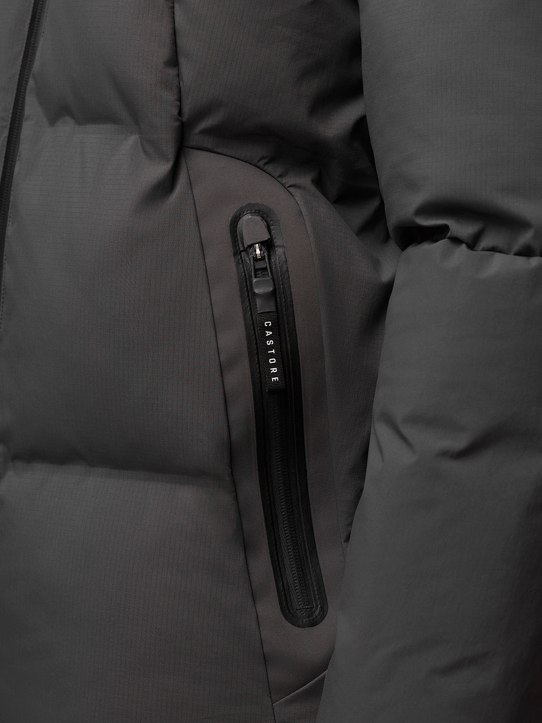 Close-up of a charcoal jacket pocket with vertical zip and Castore branding on the zipper pull.