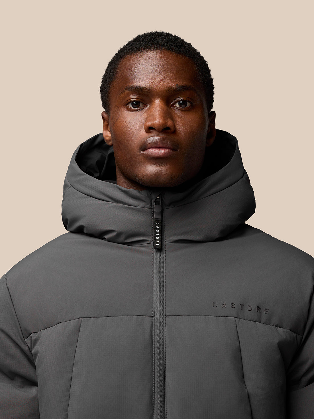 Male model wearing charcoal Castore puffer jacket with hood, front view.