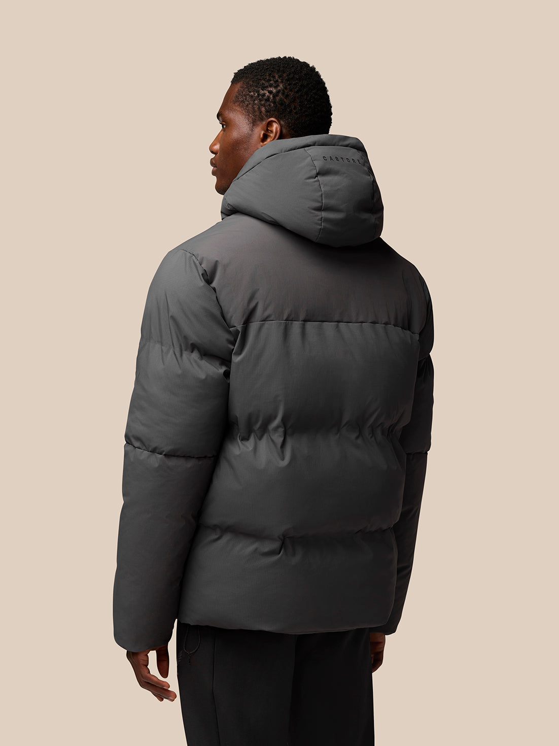 Rear view of model wearing charcoal puffer jacket with hood, CASTORE branding on the hood.