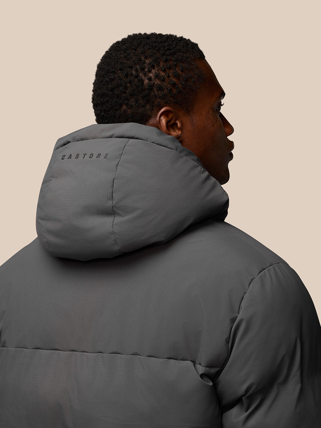 Rear three-quarter view of model in charcoal puffer jacket with hood, CASTORE branding on the hood.