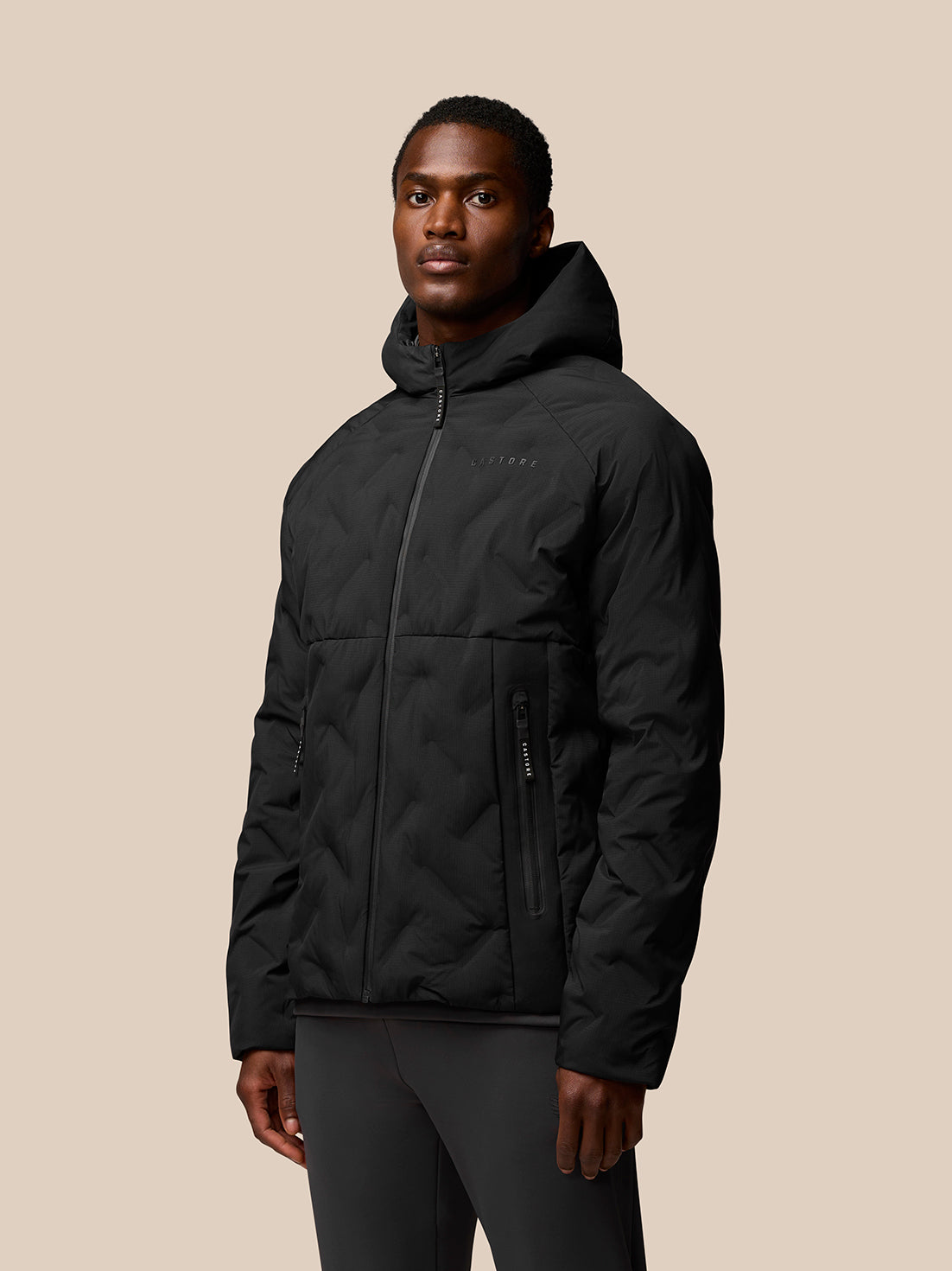 Model wearing black padded jacket with front zipper and side zip pockets Castore branding on left chest.