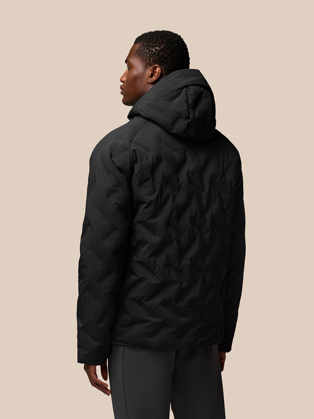Back view of black padded jacket with attached hood on a male model.