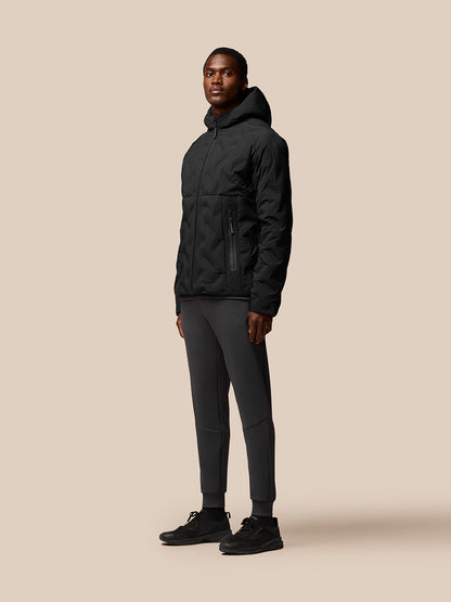 Full-body side view of a man in a black padded Castore jacket with hood paired with dark joggers and sneakers