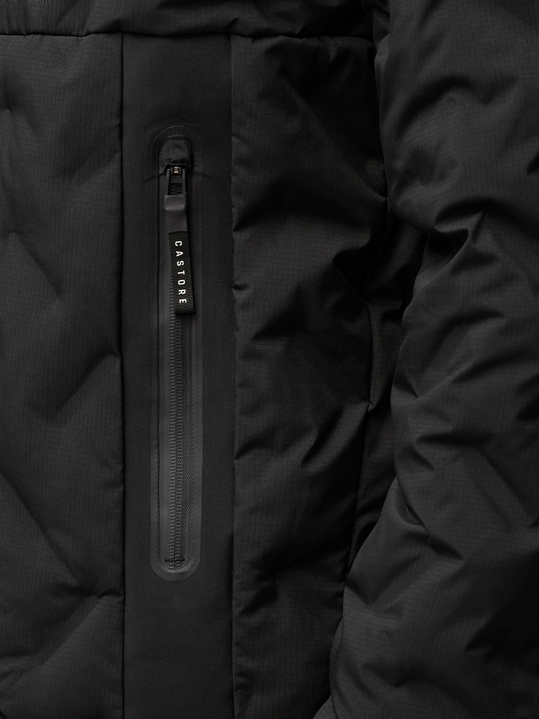 Close-up of a vertical zip pocket on a black padded jacket with Castore branding on the zipper pull