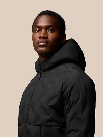 Model wearing black padded hooded jacket with front zip and external zipped pockets; Castore logo on chest and ProTek branding on sleeve