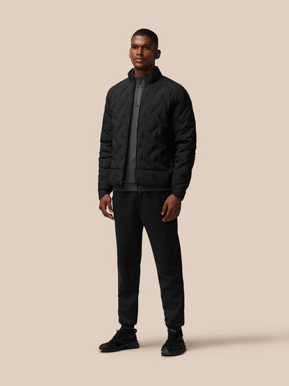 Three quarter rear view of black padded jacket worn by male model with quilted texture and ribbed hem
