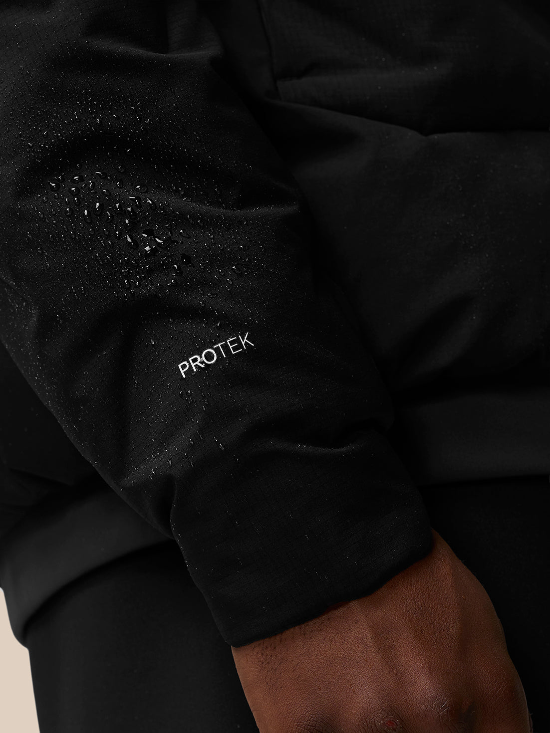Black padded jacket sleeve with Protek branding and water droplets on the fabric.