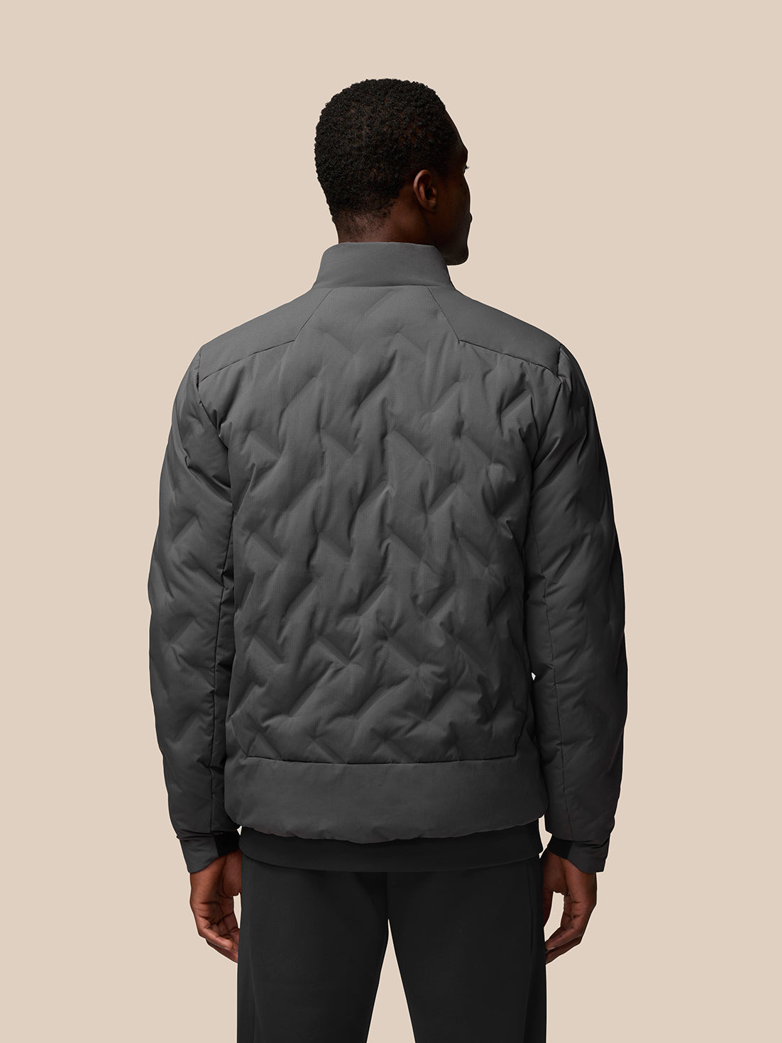 Back view of charcoal padded jacket on a model, displaying a quilted chevron pattern and high collar.
