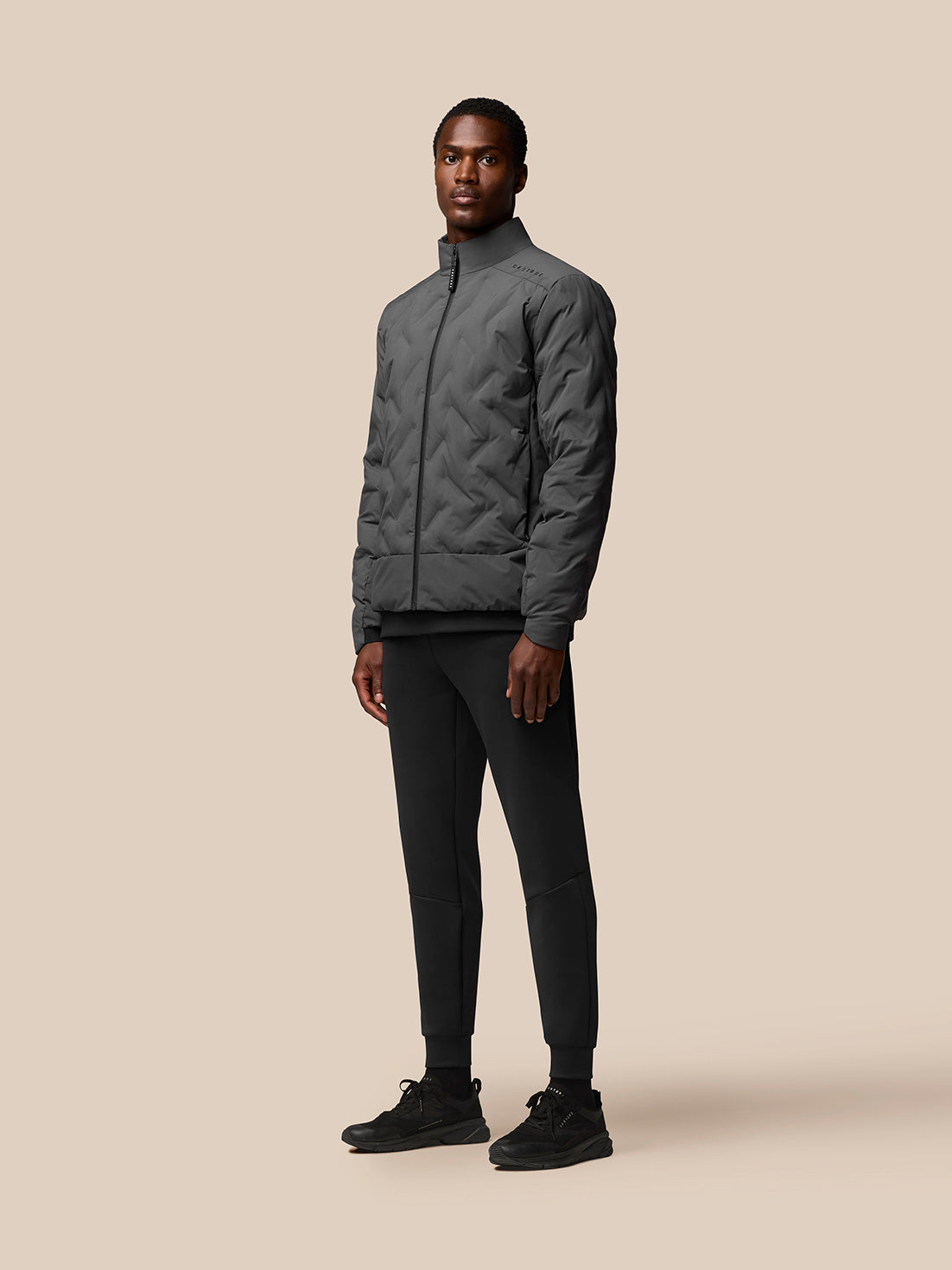 Male model wearing charcoal padded jacket with stand collar and full front zip.