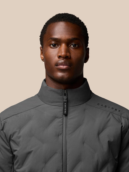 Close-up of a male model in a charcoal padded jacket with zip front and high collar showing Castore branding on the chest.