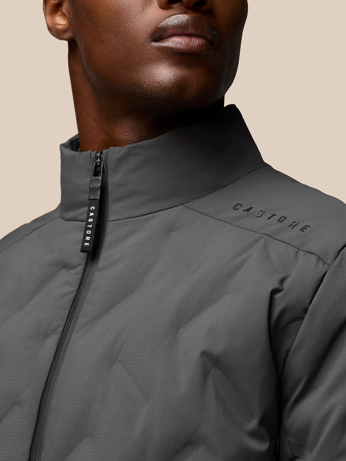 Close up of stand collar and zipper on charcoal padded jacket with Castore branding on the shoulder.