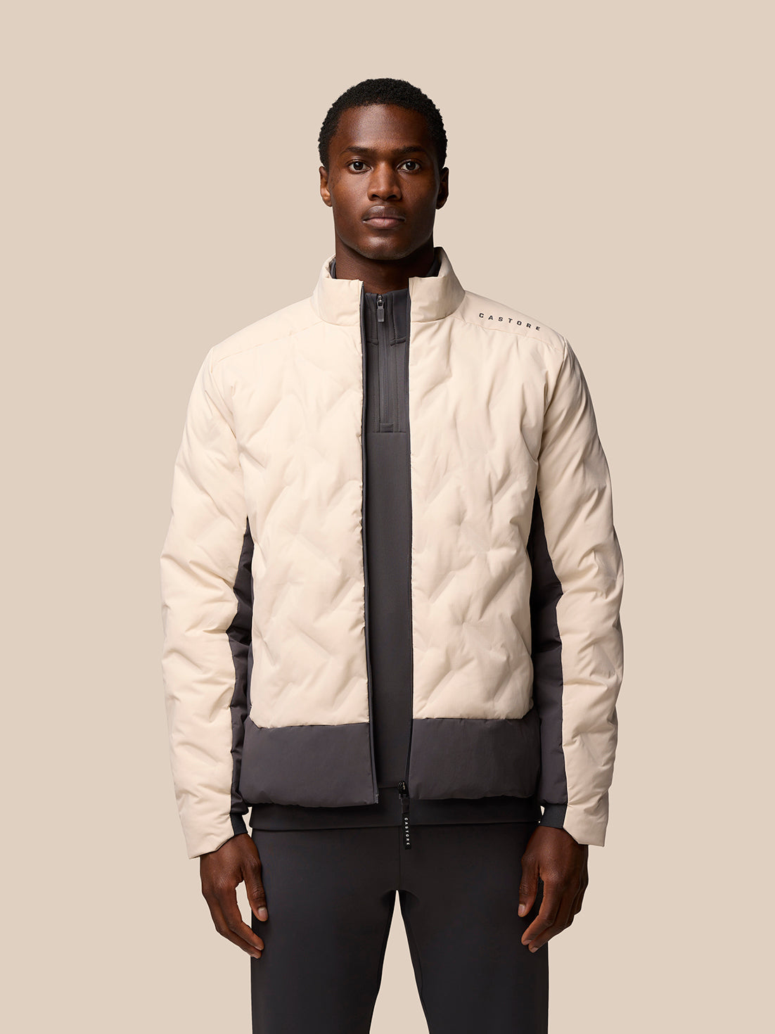 Beige padded jacket on a model with color blocking and Castore branding on the left shoulder