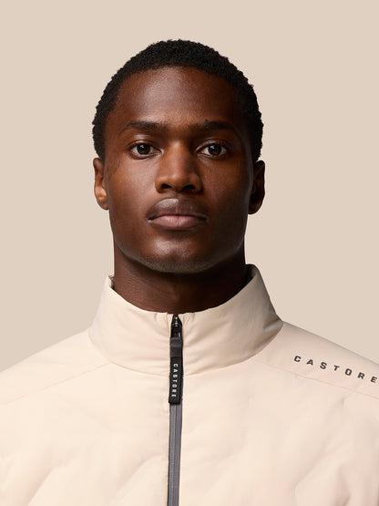 Male model wearing beige padded jacket with center zip and Castore branding on the shoulder