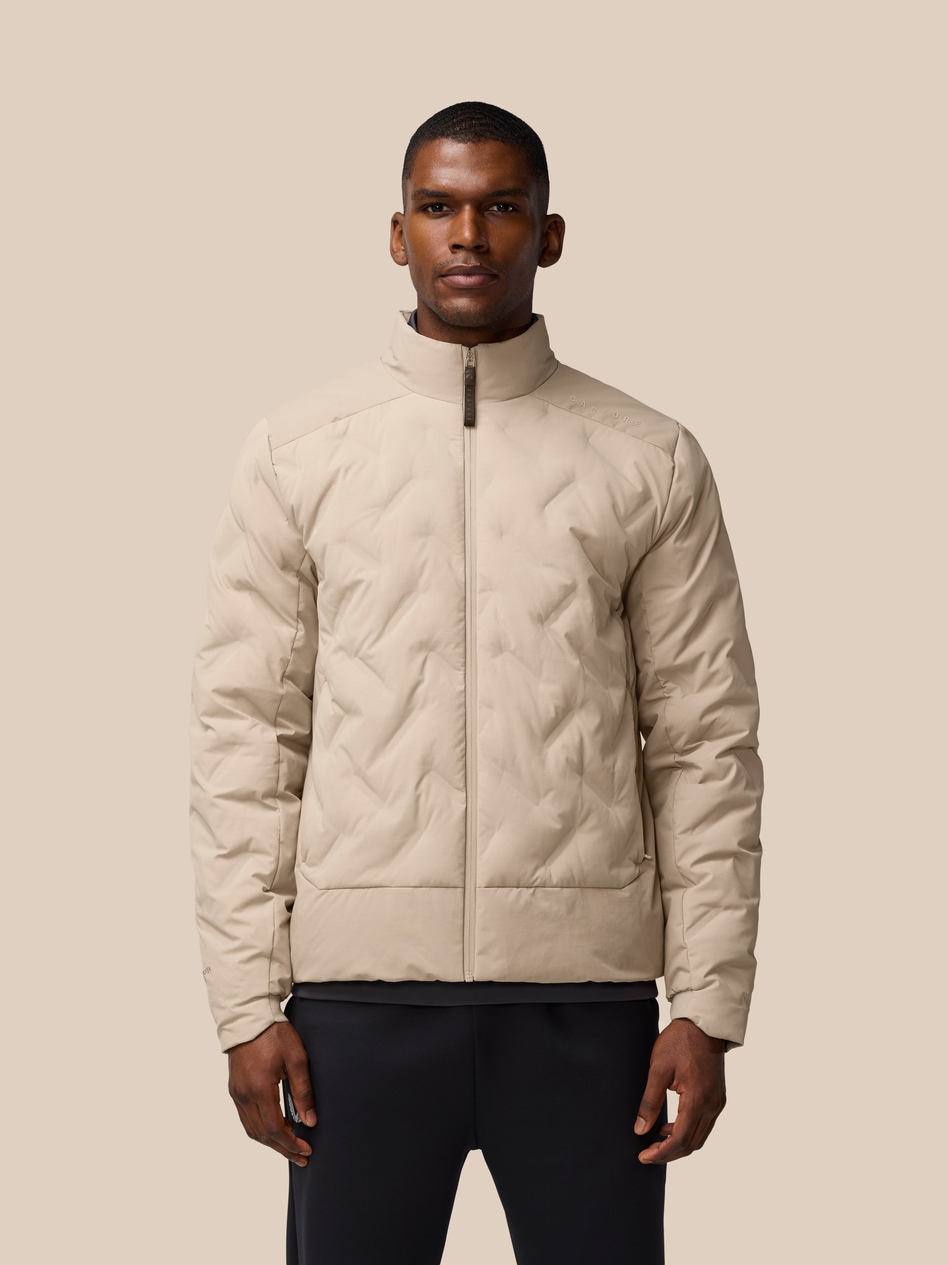 Man wearing mushroom colored padded jacket with zip front and high collar